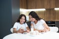 Beautiful young mother with her cute teenager daughter watching photoes on the phone while having cupcakes with milk for Royalty Free Stock Photo