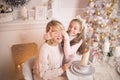 Beautiful young mother with her daughter in the New Year`s interior at the table near the Christmas tree. Royalty Free Stock Photo