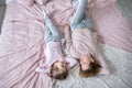 Beautiful young mother and her little daughter are lying together on the bed in the bedroom, playing, hugging and having fun.