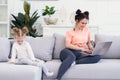 Young pretty mother and her little happy daughter are using a laptop and smiling while sitting on sofa at home Royalty Free Stock Photo
