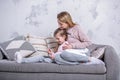 Beautiful young mother and her little daughter are watching movies together, playing on the tablet and laughing while sitting on Royalty Free Stock Photo