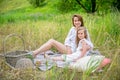 Beautiful young mother and her little daughter in white dress having fun in a picnic. They are sitting on a plaid, hugging and