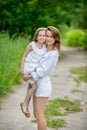 Beautiful young mother and her little daughter in white dress having fun in a picnic. They stand on a road in the park, mom holds