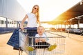 Happy beautiful young mother and little child in a shopping cart walking with shopping bags in the city on the background of a