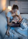 Beautiful young mother reading book to her baby in bed at night Royalty Free Stock Photo