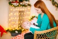 Beautiful young mother with red hair  holds a baby in her arms at home in a room decorated with Christmas garlands, needles. Royalty Free Stock Photo