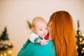 Beautiful young mother with red hair  holds a baby in her arms at home in a room decorated with Christmas garlands, needles. Royalty Free Stock Photo