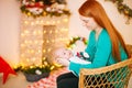 Beautiful young mother with red hair  holds a baby in her arms at home in a room decorated with Christmas garlands, needles. Royalty Free Stock Photo