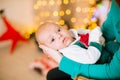 Beautiful young mother with red hair  holds a baby in her arms at home in a room decorated with Christmas garlands, needles. Royalty Free Stock Photo