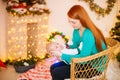 Beautiful young mother with red hair  holds a baby in her arms at home in a room decorated with Christmas garlands, needles. Royalty Free Stock Photo