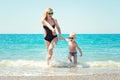 Beautiful young mother and small son holding hands running on the waves on the beach.