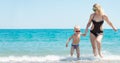 Beautiful young mother and small son holding hands running on the waves on the beach.Fun,family,friendly summer vacation. Royalty Free Stock Photo