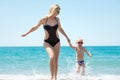 Beautiful young mother and small son holding hands running on the waves on the beach.Fun,family,friendly summer vacation. Royalty Free Stock Photo