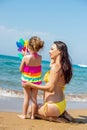 Beautiful young mother in a swimsuit and a small 3 year old daughter with a multi-colored pinwheel rainbow on the sandy beach at Royalty Free Stock Photo