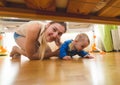 Beautiful young mother with toddler boy lying on floor and looking under the bed Royalty Free Stock Photo