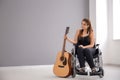 Beautiful young musician with guitar sitting in wheelchair indoors Royalty Free Stock Photo