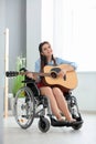 Beautiful young musician in wheelchair playing guitar at home Royalty Free Stock Photo