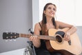 Beautiful young musician in wheelchair playing guitar indoors Royalty Free Stock Photo