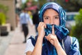 Beautiful young muslim woman wearing blue colored hijab and backpack, posing while covering half of face making silence Royalty Free Stock Photo