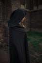 Beautiful young nun in black cassock and hooded cloak with cross