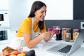 Beautiful young nutritionist woman having an online video call via laptop computer with a friend in the kitchen at home Royalty Free Stock Photo