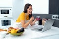 Beautiful young nutritionist woman having an online video call via laptop computer with a friend in the kitchen at home Royalty Free Stock Photo