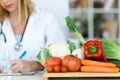 Beautiful young nutritionist working at desk and writing medical records over fresh fruit in the consultation.