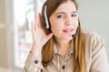 Beautiful young operator woman wearing headset at the office smiling with hand over ear listening an hearing to rumor or gossip Royalty Free Stock Photo