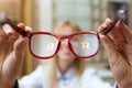 Beautiful young ophthalmologist holding eyeglasses for prove to customer in optic shop