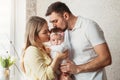 Beautiful young parents kiss their baby girl in a bright room