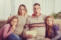 Beautiful young parents and their children are watching TV, eating popcorn and sitting on couch at home Royalty Free Stock Photo