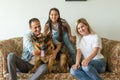 Beautiful young parents, their cute little daughter looking at camera and smiling, sitting with their cute dog on sofa Royalty Free Stock Photo