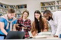 Beautiful young people in casual clothes, students, friends, working together in modern library, using a laptop, talking Royalty Free Stock Photo