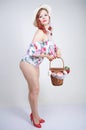 Beautiful young pin up caucasian girl in romantic fashionable straw hat, vintage swimsuit with flowers and retro wicker basket pos Royalty Free Stock Photo