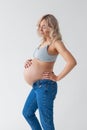 Beautiful young pregnant blonde woman in blue jeans and a top for feeding a baby stands and strokes a big belly Royalty Free Stock Photo