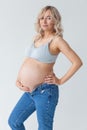 Beautiful young pregnant blonde woman in blue jeans and a top for feeding a baby stands and strokes a big belly