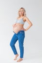 Beautiful young pregnant blonde woman in blue jeans and a top for feeding a baby stands and strokes a big belly Royalty Free Stock Photo