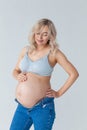 Beautiful young pregnant blonde woman in blue jeans and a top for feeding a baby stands and strokes a big belly Royalty Free Stock Photo