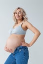 Beautiful young pregnant blonde woman in blue jeans and a top for feeding a baby stands and strokes a big belly Royalty Free Stock Photo