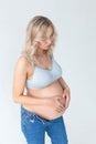 Beautiful young pregnant blonde woman in blue jeans and a top for feeding a baby stands and strokes a big belly