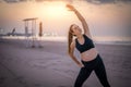 Beautiful young pregnant woman in black sportswear stretching on the sand beach with sunset over ocean in the background Royalty Free Stock Photo