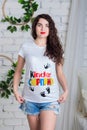 Beautiful young pregnant woman with curly hair in a t-shirt with a Kinder Surprise print poses in the Studio