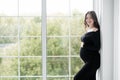 beautiful young pregnant woman in dark black dress stands near the window Royalty Free Stock Photo