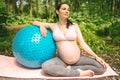 Beautiful young pregnant woman doing exercising with fitness pilates blue ball in park outdoor. Sitting and relaxing on pink yoga Royalty Free Stock Photo