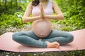 Beautiful young pregnant woman doing yoga exercising in park outdoor. Sitting and relaxing on pink yoga mat. Active future mother Royalty Free Stock Photo