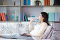 Beautiful young pregnant woman drinking water from plastic bottles and sitting on sofa at living room. Relax, rest time concept Royalty Free Stock Photo