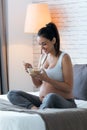 Beautiful young pregnant woman eating cereals flakes while sitting on the bed at home Royalty Free Stock Photo