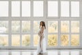 Beautiful young pregnant woman with fashionable hairstyle in a stylish peignoir smiling and posing near the big window Royalty Free Stock Photo