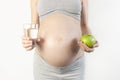 Beautiful young pregnant woman holding green apple and glass of water in her hands on white background. The concept of expectation Royalty Free Stock Photo