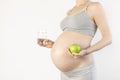 Beautiful young pregnant woman holding green apple and glass of water in her hands on white background. The concept of expectation Royalty Free Stock Photo